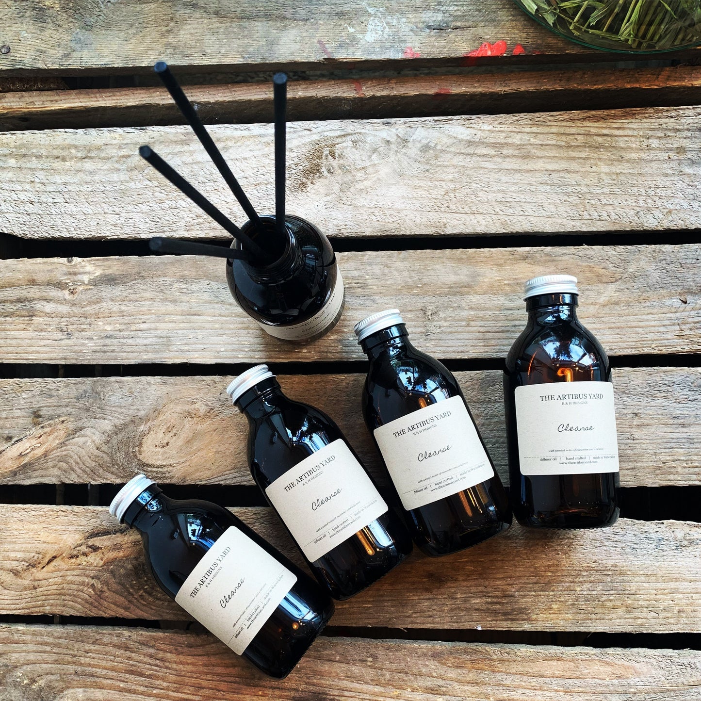 Happiness reed diffuser by The Artibus Yard, with rhubarb, rose and musk notes, housed in an amber glass bottle with black reed sticks for long-lasting fragrance.