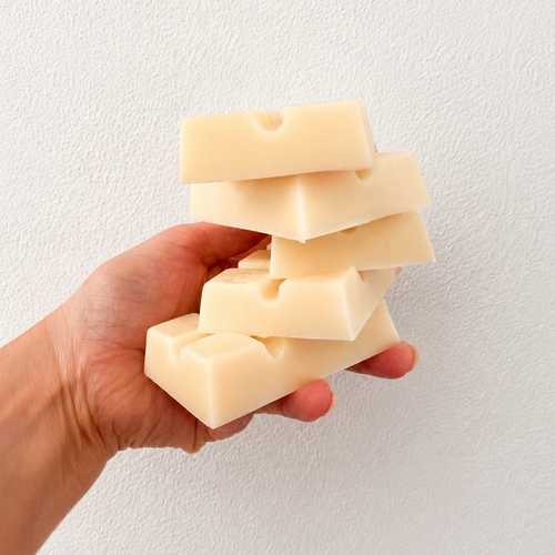 Hand holding a stack of beige wax melt bars against a white background