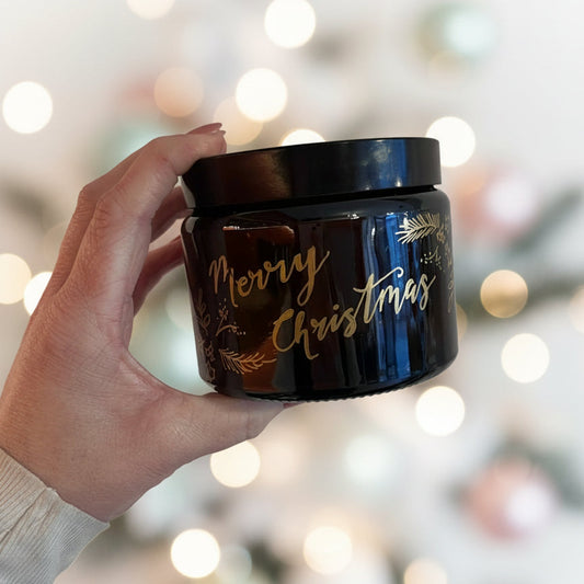 Hand holding a black container with 'Merry Christmas' text against a blurred festive background
