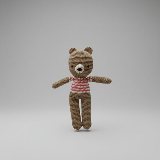 Hand holding a small crocheted teddy bear with a striped shirt against a plain background