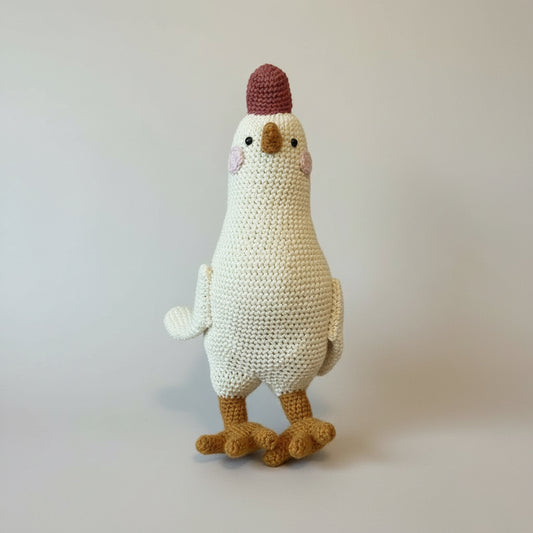 Hand holding a knitted chicken toy against a wooden background