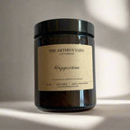 Hand-poured Happiness soy wax candle by The Artibus Yard, featuring notes of rhubarb, rose and musk; crafted in small batches in Warwickshire and poured into a reusable amber glass jar.