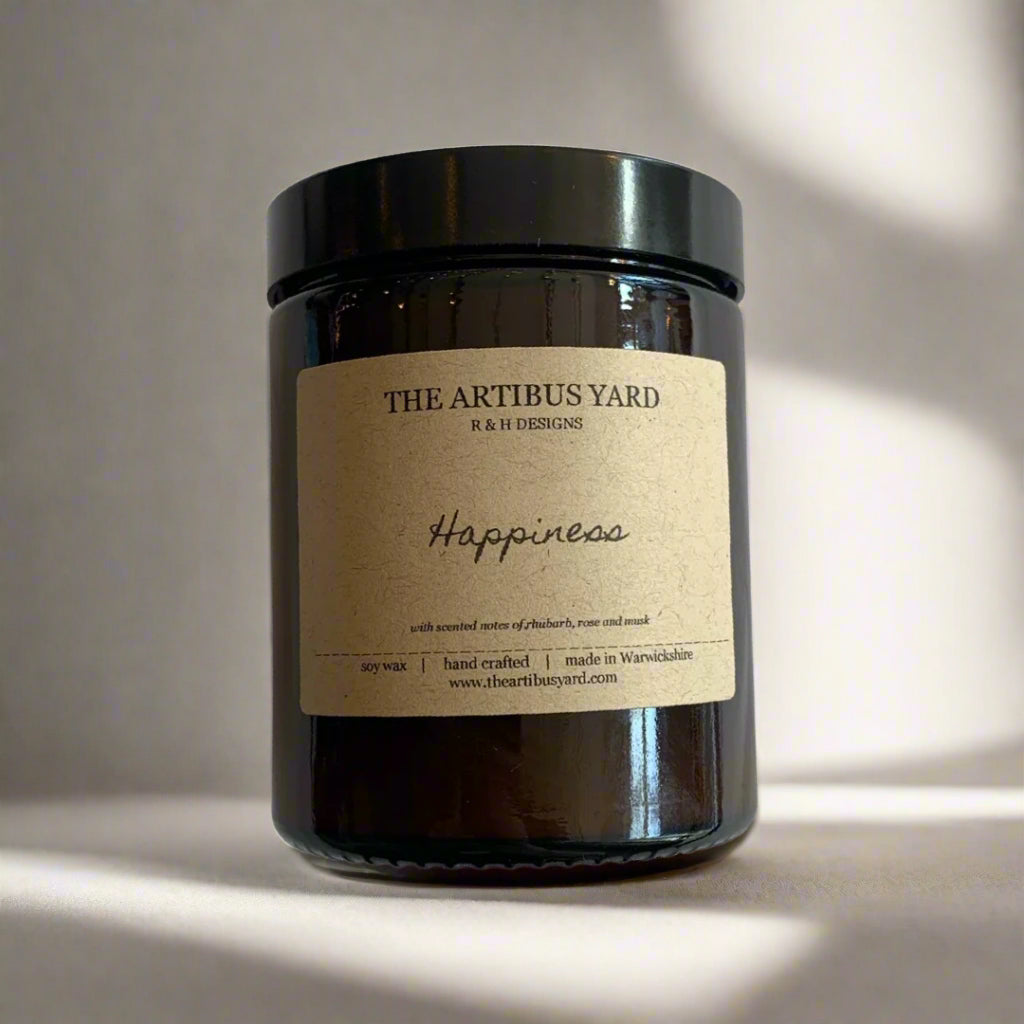 Hand-poured Happiness soy wax candle by The Artibus Yard, featuring notes of rhubarb, rose and musk; crafted in small batches in Warwickshire and poured into a reusable amber glass jar.